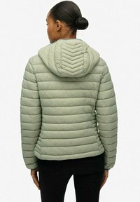 Lys grøn polstret jakke med hætte, med horisontal quilte og et chevronmønster på hætten. Tekstureret stoff, slank pasform.
