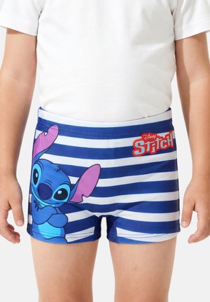 Enfant portant un short de bain rayé bleu et blanc avec un grand personnage Stitch et un logo rouge "Disney Stitch" sur le côté droit.