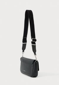 Μαύρη δερμάτινη τσάντα ώμου με φαρδιά ρυθμιζόμενη υφασμάτινη λωρίδα και ασημένιες μεταλλικές λεπτομέρειες, όρθια σε λευκό φόντο.