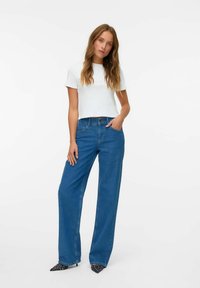 Camiseta blanca corta combinada con jeans de pierna ancha azul. Los zapatos presentan un patrón de lunares en blanco y negro con punta afilada.