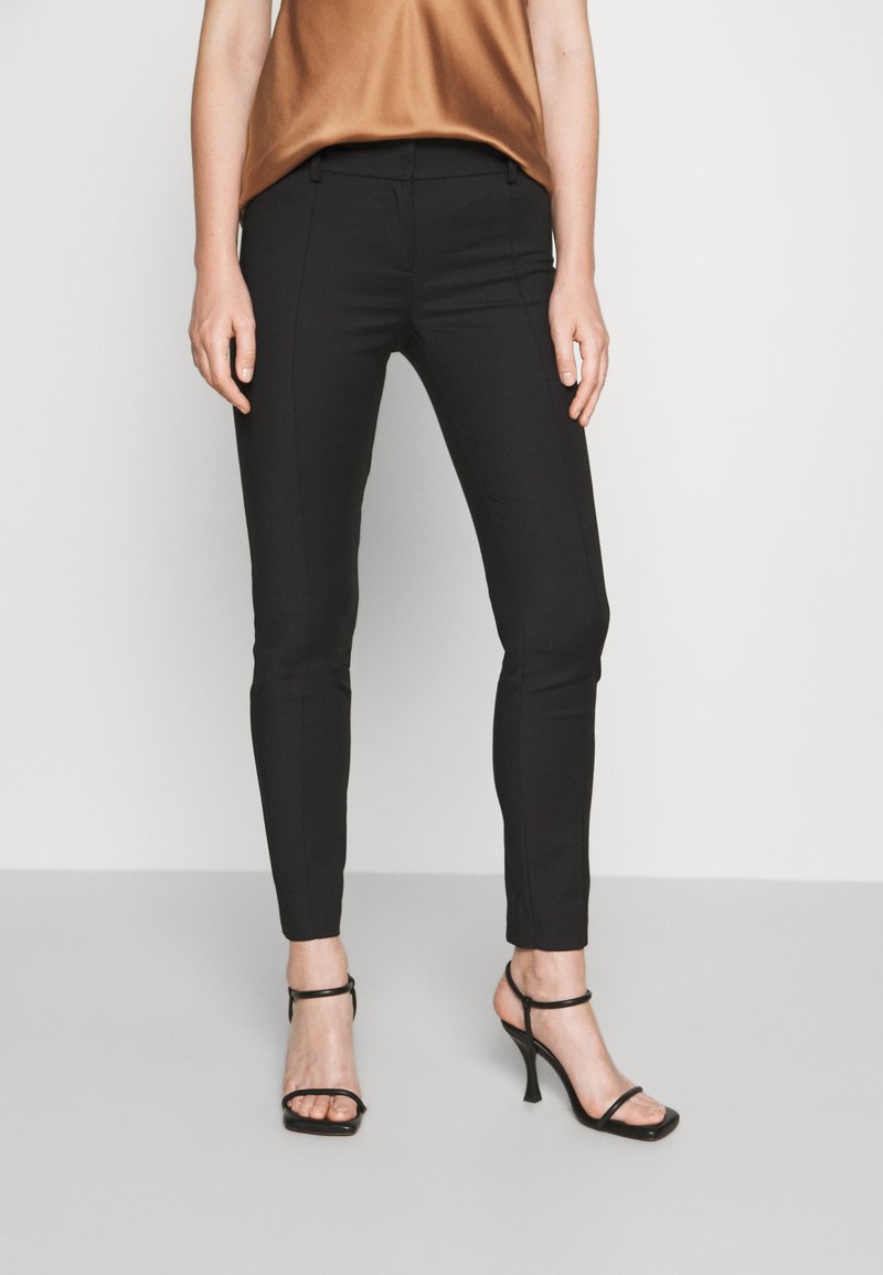 Pantaloni neri su misura realizzati in un tessuto liscio, caratterizzati da una vestibilità slim e una sottile cucitura laterale, abbinati a eleganti décolleté nere con cinturini.