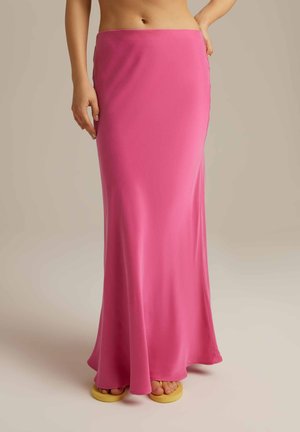 Długa, dopasowana różowa spódnica z gładkiego materiału, z boku z rozcięciem i lekko rozszerzanym dołem. Połączona z żółtymi sandałami, odsłaniającymi nagie stopy.