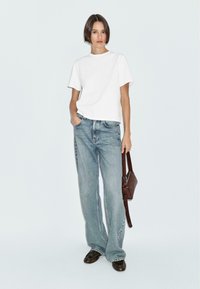 T-shirt bianco a maniche corte, jeans a vita alta di color blu chiaro con gamba larga, borsa a tracolla marrone e scarpe scure. Tessuto morbido e vestibilità casual.