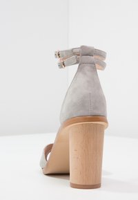 Sandalo con tacco alto in camoscio grigio dal design affusolato, punta aperta, due cinturini alla caviglia e tacco a blocco in legno naturale.