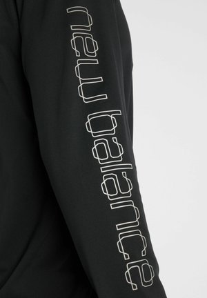 Sort langærmet skjorteærme med hvide geometriske omridsede bogstaver, der løber lodret ned langs armen.