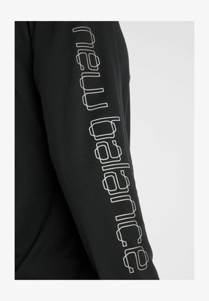 Schwarzes Langarmshirt mit weißem, geometrisch umrandetem Text, der vertikal den Arm hinunterläuft.