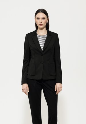 Black blazer with a structured silhouette, notch lapels, two front pockets, and single button closure, paired with a black and white striped top.