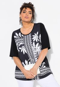 Top de estampado floral en blanco y negro con mangas cortas, escote redondo y textura de tela suave. Combinado con un pequeño bolso blanco.