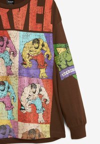 Barna, hosszú ujjú póló, amely színes képregény-stílusú nyomattal ábrázolja Hulk karaktereit, hangsúlyos "MARVEL" felirattal és texturált anyaggal.