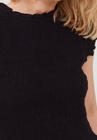 Top nero con un motivo strutturato e stropicciato. Presenta un collo rotondo con ruches e maniche corte con dettagli elasticizzati.