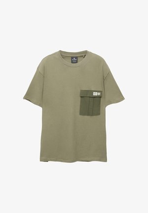 T-shirt verde oliva in morbido cotone, con una tasca rettangolare di un tono verde più scuro, dotata di un'etichetta e due bottoni a pressione.