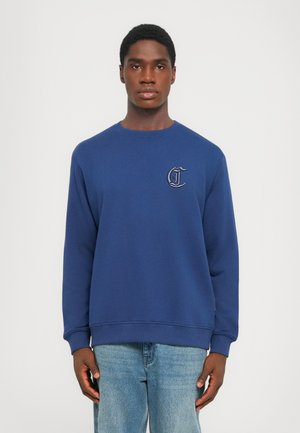 Sweatshirt bleu marine en tissu doux, avec un col rond et des manches longues. Affiche un petit logo brodé sur la poitrine.