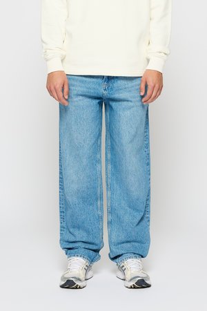 Blaue Denim-Jeans mit weitem Bein und ausgeblichenem Finish, ausgestattet mit Gürtelschlaufen und einem klassischen Fünf-Taschen-Design, kombiniert mit weißen Sneakern.