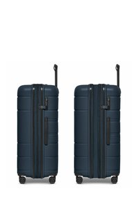 Maleta rígida en azul marino, con forma rectangular, textura acanalada, doble cremallera y mango telescópico negro con ruedas.