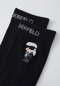 Fekete pamut zoknik, amelyekre hímzett grafikaként egy napszemüveget viselő karakter és öltöny van ábrázolva, fehér "GERFELD" felirattal a szegélyen.