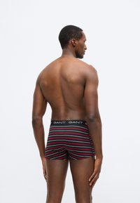 Fekete és piros csíkos boxeralsó logóval ellátott derékpánttal. Az anyag simának tűnik, és modern, testre szabott kialakítású. Egy modell viseli hátulról.