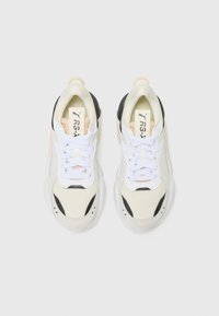 Zapatillas con parte superior en crema y negro, cordones blancos y una suela texturizada. Logo visible en la lengüeta y los laterales, con acentos de acolchado.