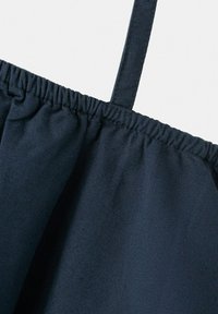Tissu bleu foncé avec un bord supérieur élastique froncé et une fine bretelle d’épaule visible sur un fond blanc.