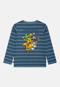 Langermet blåstripet T-skjorte med et fargerikt Ninjago-illustrasjon på baksiden, som viser tegneseriefigurer i ulike posisjoner.
