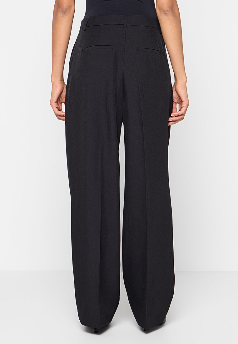 Pantaloni neri a gamba larga realizzati in un tessuto morbido, con vita alta e due tasche posteriori. Il design offre una silhouette rilassata e fluida.