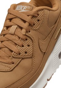 Nike tenisice od svijetlo smeđe kože s teksturiranim dizajnom, zaobljenog oblika i ravnim vezicama. Imaju tonirane šavove i bijeli gumeni đon.