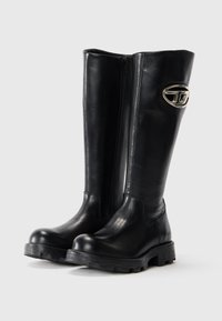Botine negre, până la genunchi, din piele netedă, cu fermoar lateral și un accent metalic cu logo pe tijă. Talpă groasă din cauciuc robust.