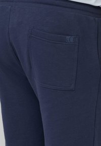 Pantalons de survêtement bleu marine avec une texture douce, dotés d'une poche arrière et d'un logo de marque subtil sur la poche. Ceinture élastique incluse.