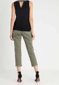 Top nero senza maniche con schiena a chiave, abbinato a pantaloni cropped verde oliva chiaro. Il modello indossa scarpe con tacco aperte nere.