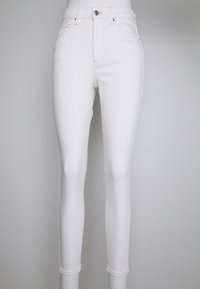 Jeans ajustados de cintura alta blancos, material de mezclilla, diseño de cinco bolsillos, corte Slim, costuras sutiles y cierre de botón metálico en la cintura.