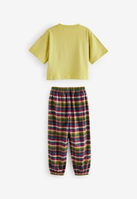 Gelbes Baumwoll-T-Shirt mit kurzen Ärmeln, kombiniert mit mehrfarbigen, karierten Pants mit elastischem Bund, die rote, grüne, gelbe und blaue Streifen aufweisen.