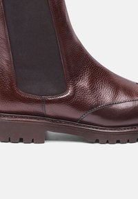 Stivale alla caviglia in pelle marrone con superficie texturizzata, pannelli laterali elasticizzati e suola robusta. Caratterizzato da un design elegante e moderno con accenti a contrasto.