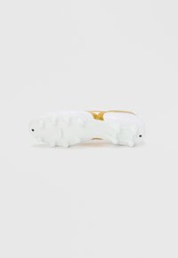 White sports shoe with gold accents, featuring a textured upper and molded rubber outsole with rounded studs for traction.