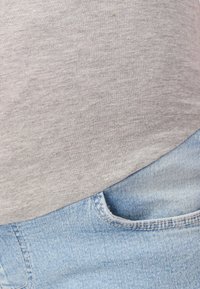 Šedé bavlněné tričko v kombinaci s světle modrými džínami. Tričko má hladkou texturu, džínsy klasický střih s viditelnou kapesní.