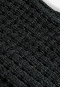 Schwarzer Strickstoff mit einer strukturierten Oberfläche, der ein gewebtes Design aus dicken, flauschigen Strängen aufweist, um Wärme und Tiefe zu erhöhen.
