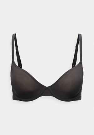 Soutien-gorge noir rembourré avec armatures, bretelles réglables à logo Calvin Klein, sur un fond gris clair uni.