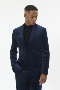 Tumesinine sametjakk ühe nupuga, sälguga krae ja rinnataskuga, kombineeritud musta kõrge kaelusega kampsuniga. Lõigatud vormis.