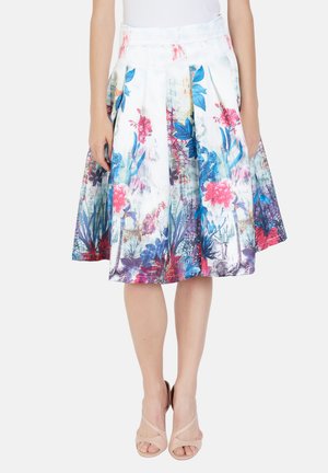 Mujer con una falda blanca hasta la rodilla con vibrantes patrones florales en azul, rosa y púrpura, combinada con sandalias nude de tacón.