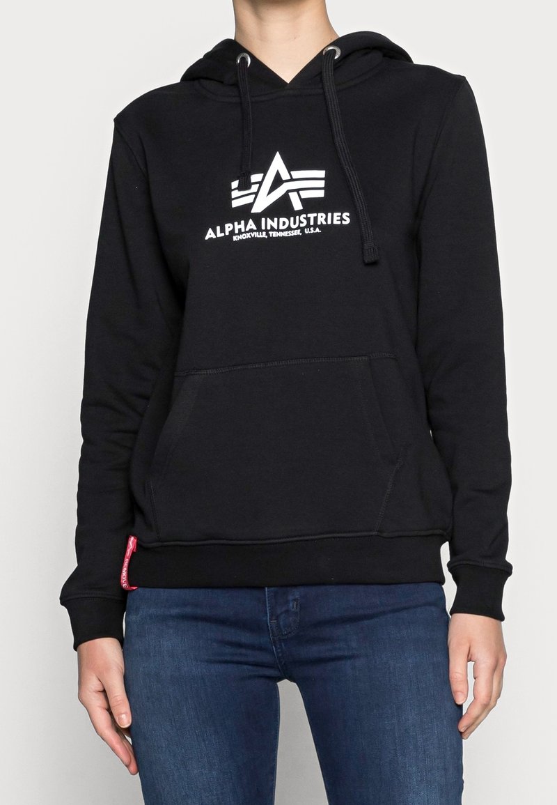 Sudadera con capucha negra con un bolsillo delantero, cordones ajustables y un logotipo blanco impreso. Presenta puños y dobladillo acanalados con un detalle de tela roja en el lateral.