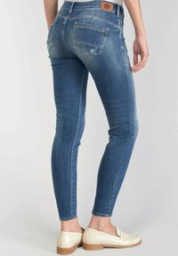 Úzké modré džínové kalhoty s bledým povrchem, zadními kapsami a hnědou koženou nášivkou na pase, stylizované s krémovými mokasíny.