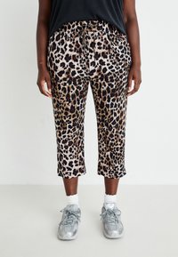 Pantalons courts à imprimé léopard en beige, dotés d'une taille à cordon et d'une texture lisse. Portés avec des baskets grises et des chaussettes blanches.