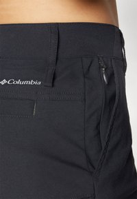 Juodai Columbia šortai su lygiu paviršiumi, turintys užtrauktuko kišenę, siuvimo detales ir logotipą ant juosmens.