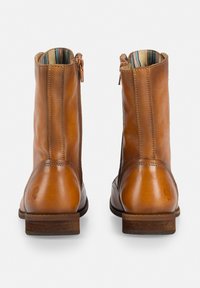 Botines de cuero marrón con un acabado suave, cremalleras laterales y un forro de tela a rayas en contraste. Presentan un taco bajo de madera.