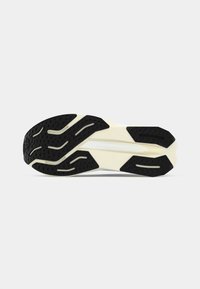 Semelle de chaussure de sport avec un motif en caoutchouc texturé noir et des accents crème. Des rainures et des formes notables pour la traction sont présentes.