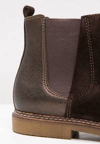 Bottine Chelsea en cuir marron avec un panneau en daim, un élastique extensible et une couture contrastée sur la semelle extérieure. Bout arrondi et finition texturée.