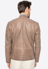 Giacca in pelle marrone con dettagli trapuntati sulle spalle e sulla schiena, texture liscia e design aderente e raffinato. Vista posteriore che mette in evidenza i dettagli delle cuciture.