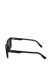 Črne sončna očala z drzno, kotno zasnovo. Imajo temna stekla in teksturirane črne ročaje z modro poudarjeno črto. Na strani je logotip Lacoste.