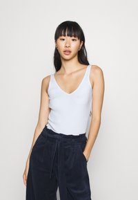 Tajt ljusblå ribbad linne med V-ringning, kombinerat med marinblå kordflöjelbyxor med vid ben som har knytning i midjan.