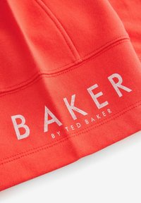 Punainen puuvillaneule, jossa on tekstuuri ja rohkeat valkoiset tekstit, joissa lukee "BAKER by TED BAKER", näkyvillä ompelusaumalla.
