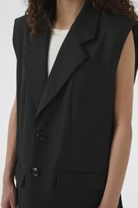 Sacou negru fără mâneci, cu revere decupate, două nasturi și un buzunar lateral; confecționat dintr-un material neted și structurat.