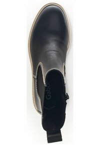 Botín negro de cuero con paneles laterales elásticos, suela beige y costuras decorativas. Presenta una lengüeta para facilitar su uso.